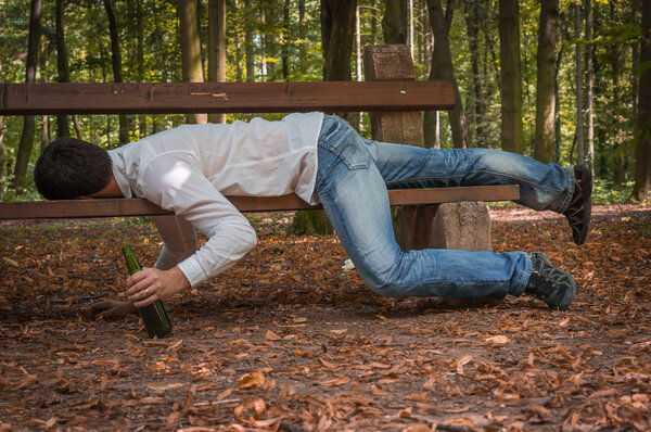 Пьяный мужчина спит на скамейке в парке с пивными бутылками
