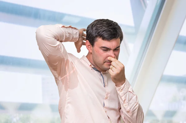 El hombre con sudoración bajo la axila pellizca la nariz con los dedos — Foto de Stock