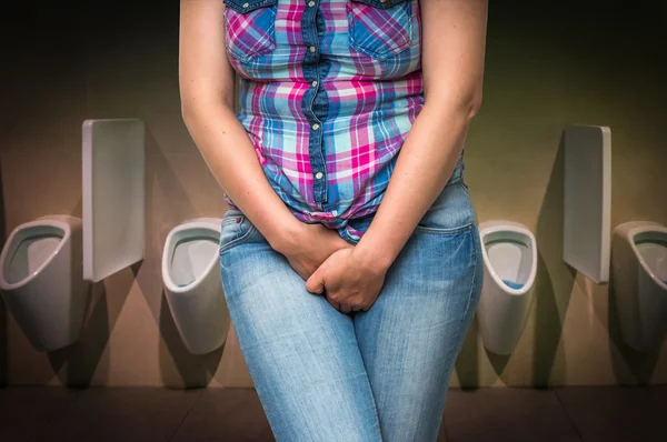 Mulher com as mãos segurando sua virilha no banheiro público dos homens — Fotografia de Stock