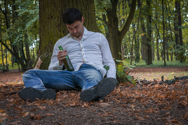 Пьяный лежит на земле под деревом с пивной бутылкой.
