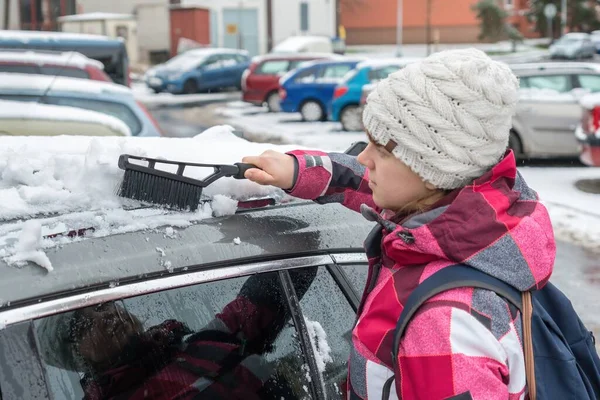 Female driver is cleaning snow with brush from the car roof