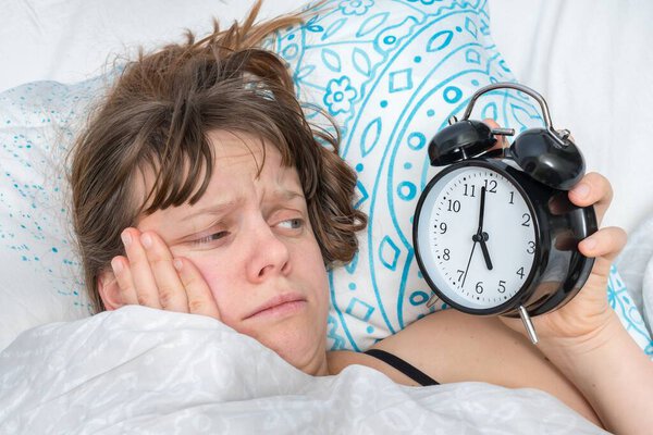 Уставшая женщина с будильником не хочет просыпаться рано