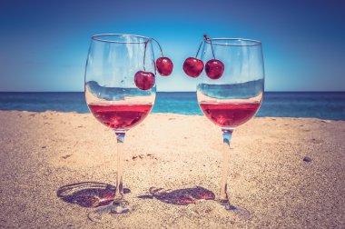 Glasses of wine and cherries on the beach - retro and vintage st