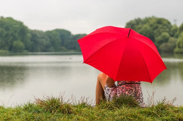 Mädchen mit rotem Regenschirm sitzt am Teich — Stockfoto