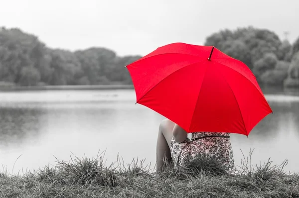 Mädchen mit rotem Regenschirm sitzt am Teich — Stockfoto