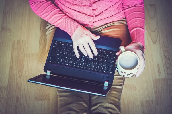 Young student with a cup of coffee using a laptop and sitting on the wooden floor in a classroom — Φωτογραφία Αρχείου