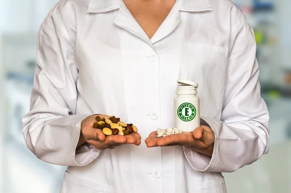 Joven médico sosteniendo nueces y frasco de pastillas con vitamina E, compararlos — Foto de Stock