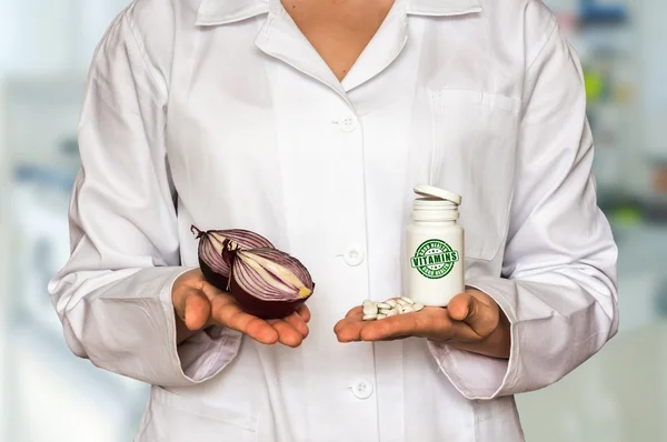 Jeune médecin tenant deux moitiés d'oignon et une bouteille de pilules avec des vitamines et les comparer — Photo