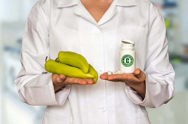 Jovem médico segurando pimenta e garrafa de pílulas com vitamina C — Fotografia de Stock