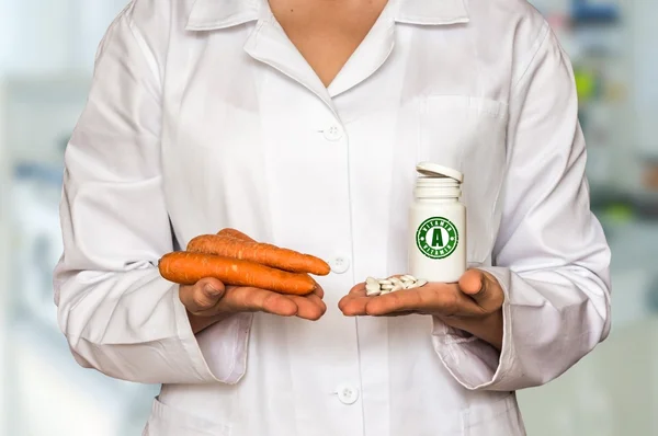 Jeune médecin tenant des carottes et une bouteille de pilules avec de la vitamine A — Photo