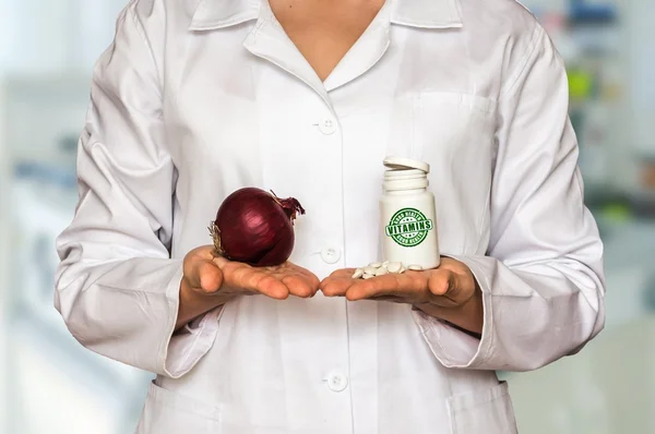 Junger Arzt hält Zwiebel und Flasche Pillen mit Vitaminen und vergleicht sie — Stockfoto