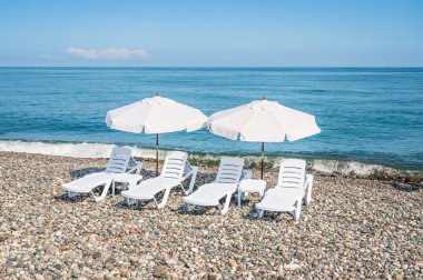 Dört beyaz plastik sandalye ve iki beyaz şemsiye üzerinde olması