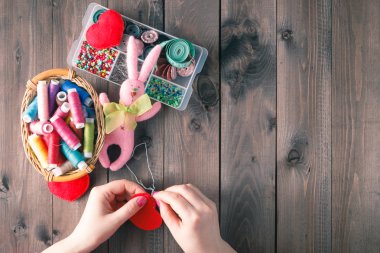 Woman sews red heart shaped toy by needle