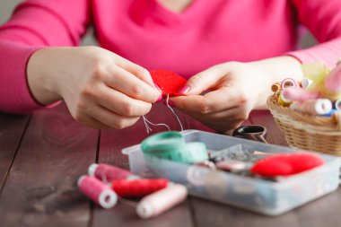 Woman sews red heart shaped toy by needle