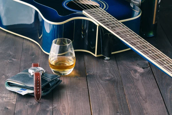 Guitar, money and whiskey on wooden table
