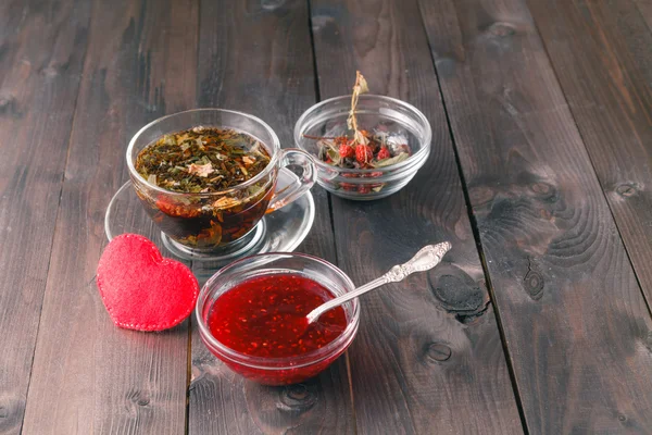 Малиновое варенье на столе с чашкой травяного чая — стоковое фото