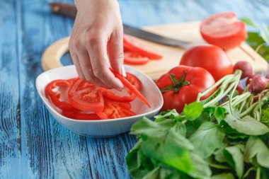 Kadın elleri taze sebzelerin arkasında domates kesiyor..