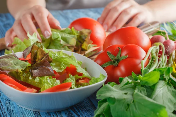 Руки женщины добавляют листья салата в миску с салатом, близко-у — стоковое фото