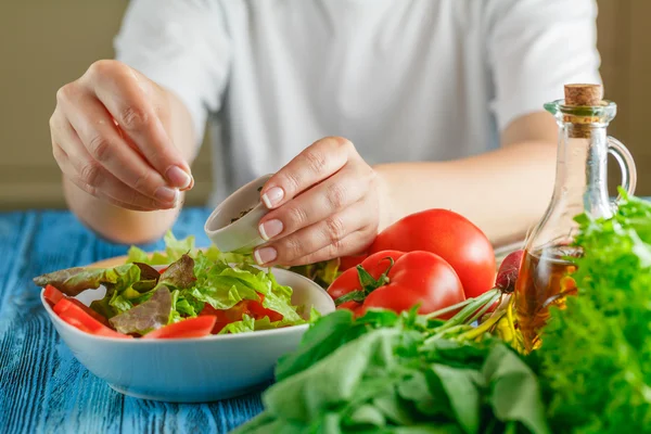 As mãos de mulher acrescentam temperos de uma salada vegetal — Fotografia de Stock