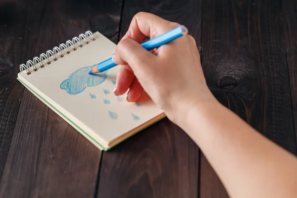 Kvinnan ritning blå regn i anteckningsboken — Stockfoto