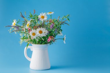 düz mavi zemin üzerine kavanoza kır çiçekleri buketi