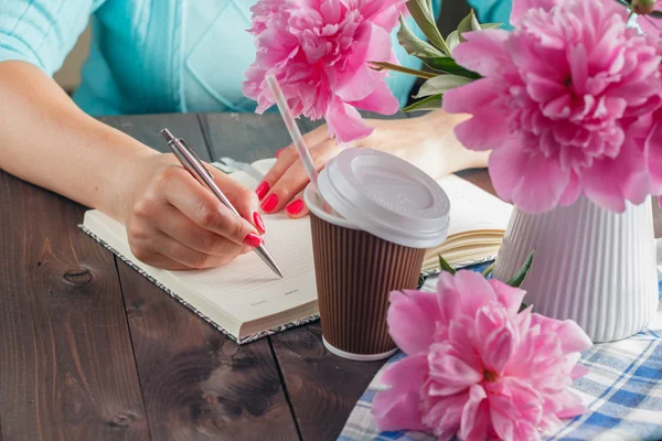 Женщина пишет в блокноте, цветы на столе — стоковое фото
