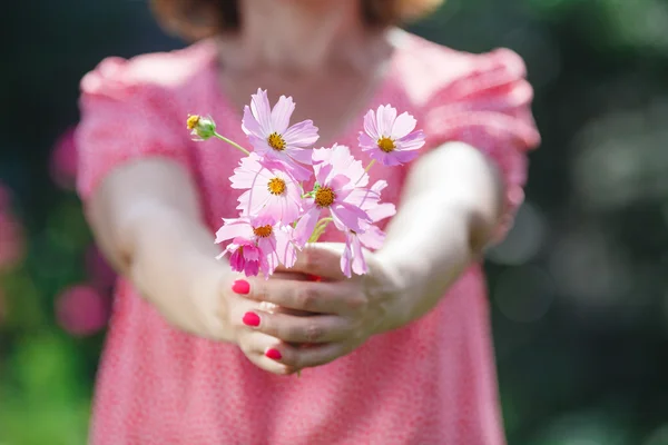 Manos de mujer sosteniendo una flor en prado verde — Foto de Stock