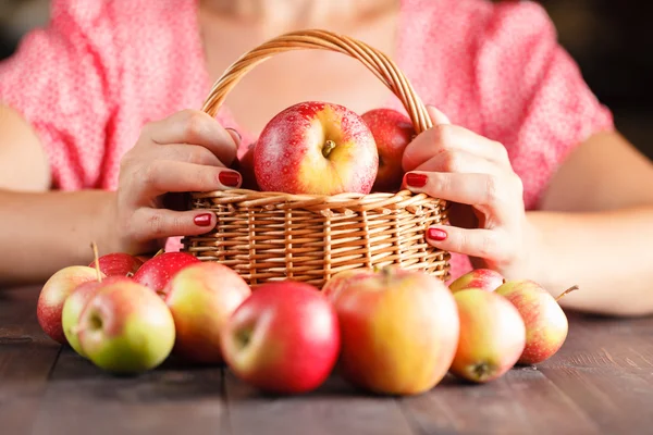 Mujer sostiene una cesta de mimbre llena de manzanas rojas — Foto de Stock