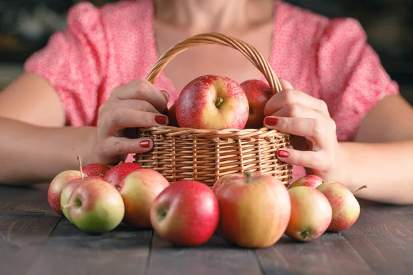 Mujer sostiene una cesta de mimbre llena de manzanas rojas — Foto de Stock