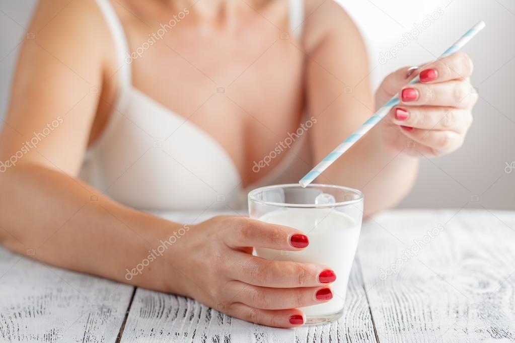 Woman drinking glass of milk with straw sitting in kitchen at ho