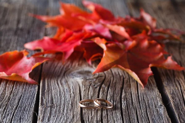 Queda em folhas na mesa resistida com anéis de casamento — Fotografia de Stock