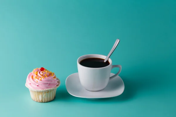 Cupcake rosa colorido sobre fondo aguamarina con taza de café — Foto de Stock