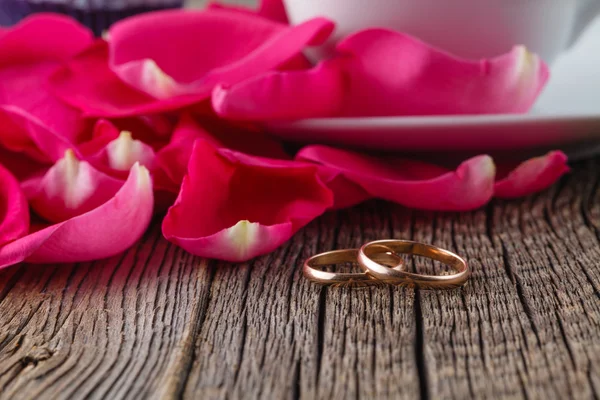 Złote pierścienie i płatki róż na rustykalnym drewna — Zdjęcie stockowe