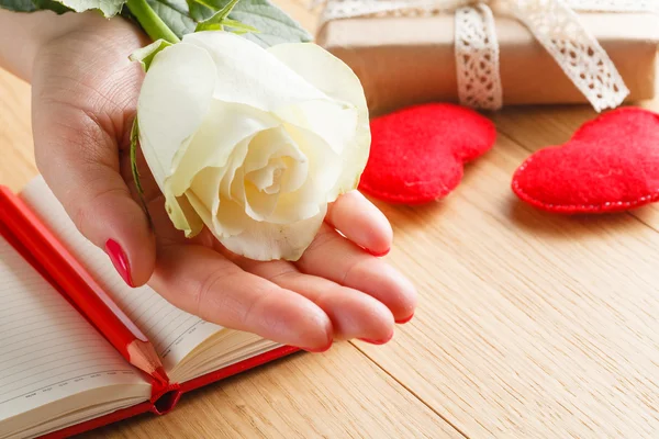 Hand holding white rose on open notebook and hearts — Stock Photo, Image