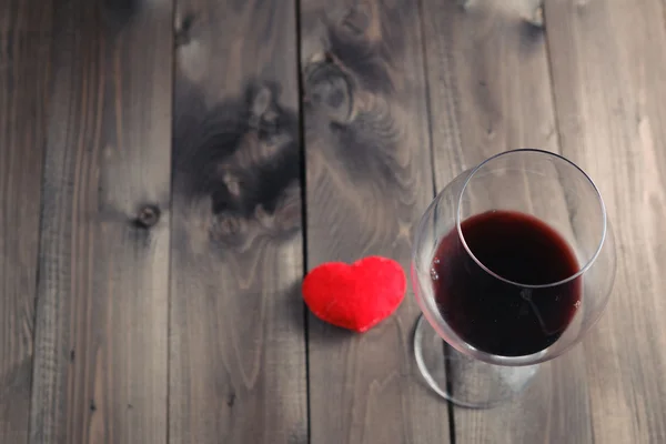 Kieliszek czerwonego wina na drewnianym stole i serca — Zdjęcie stockowe