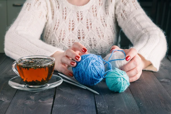 Woman hands with cup of tea and wool yarn balls on a wooden tabl — Stock Photo, Image