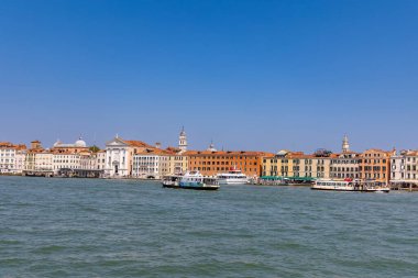 Venedik, İtalya, 11 Ağustos 2025 Venedik 'in tekneli panoramik manzarası. Renkli tarihi binalar, Venedik rıhtımının altında açık mavi bir gökyüzü, Büyük Kanal 'da botlar ve vaporetto feribotları var..