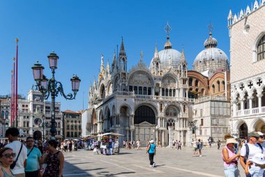Venedik, İtalya, 11 Ağustos 2025: Venedik 'teki St. Marks Bazilikası' nda turistler. Venedik 'teki ikonik St. Marks Bazilikası yakınlarında tarihi mimari ve parlak gökyüzü ile çevrili bir sürü turist yürüyüp alışveriş yapıyor..