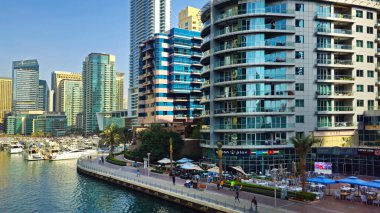 Dubai, BAE, 23 Aralık 2025: Dubai Marina 'daki modern rıhtım güvertesi. Dubai Marina 'nın manzaralı manzarası. Yüksek binalar, sahil restoranları, lüks yatlar ve gezinti güvertesi boyunca yürüyen insanlar.