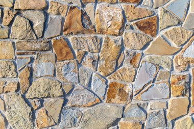 Kırsal taş duvar dokusu arka planı. Düzensiz bir doğal taştan duvara yakın çekim, sıcak toprak tonları ve görünür havan topu, inşaat, mimari veya doku aramaları için idealdir.