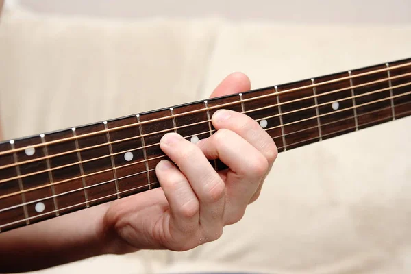 A young man plays the guitar. He holds the strings with his fingers.