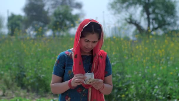 女性農業労働者は喜んでフィールドに立って彼女の収入を数える インドの農家 500ルピーとインド通貨と親指アップジェスチャーを示すデュパッタを持つ村の中程度のショット — ストック動画