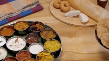 Güney Hint Thali yakınlarında Dosa 'lı bir tabak kızarmış Poori saklayan kadın eller. Yakın çekim vejetaryen Thali 'yi limonlu pirinç, Sambhar, Chutneys, Payasam, Idli, Medu Vada gibi yiyeceklerle masaya yatırdık.