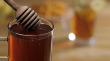 Temiz bir bardak nektarın içindeki ahşap bal kovanı bulanık bir arka planda. Bal kaşığından damlayan sağlıklı organik balın yakın plan çekimi - doğal taze yiyecek