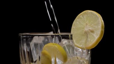 Temiz bir bardakta büyük buz parçalarıyla sağlıklı taze limon kabağı dökülüyor. İçinde limon dilimleri olan bir limonata bardağının aşırı yakın plan görüntüsü.
