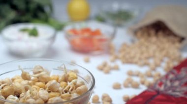 Taze doğranmış domates ve soğan filizlenmiş gram kasesinin içine düşüyor. Limonlu kuru bezelye çuvalı, bulanık arkaplanda yeşil biber.
