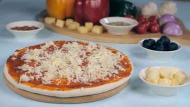Taze pişmiş bir pizzaya rendelenmiş peynir düşüyor. İtalyan mutfağı hazırlıyor. Yakın çekim peynir küpleri, siyah zeytin, kekik ve biber taneleri ahşap bir masada bir arada tutulur.