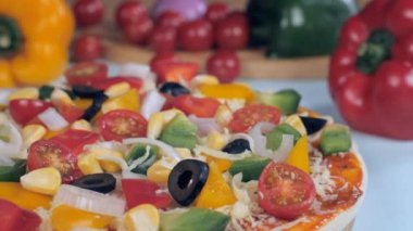 Lezzetli ev yapımı bir pizzanın üzerine fırında peynir düşüyor. İtalyan yemeği. Biberli, mısırlı, zeytinli ve vişneli domatesli vejetaryen pizzasının aşırı yakın plan çekimi.