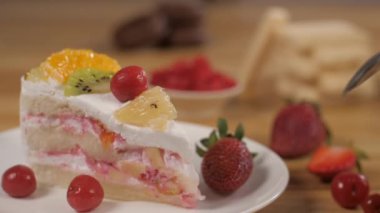  Kadının eli bir kaşık dolusu kremalı kek alıyor. Lezzetli bir tatlı. Lezzetli ananas, kiraz, kivi, portakal ve çilek parçalarıyla süslenmiş taze meyve pastası.