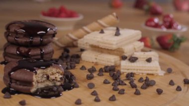 Bayan aşçı lezzetli kremalı kurabiyeleri kırmızı çilekle süslüyor. Yakından çekilen gofret tüpleri, çikolatalı turta ve kırmızı kirazlar ahşap bir masada bir arada duruyordu.